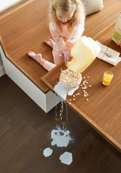 A little girl pouring milk into a bowl with the milk running down to the durable kid-friendly kitchen flooring